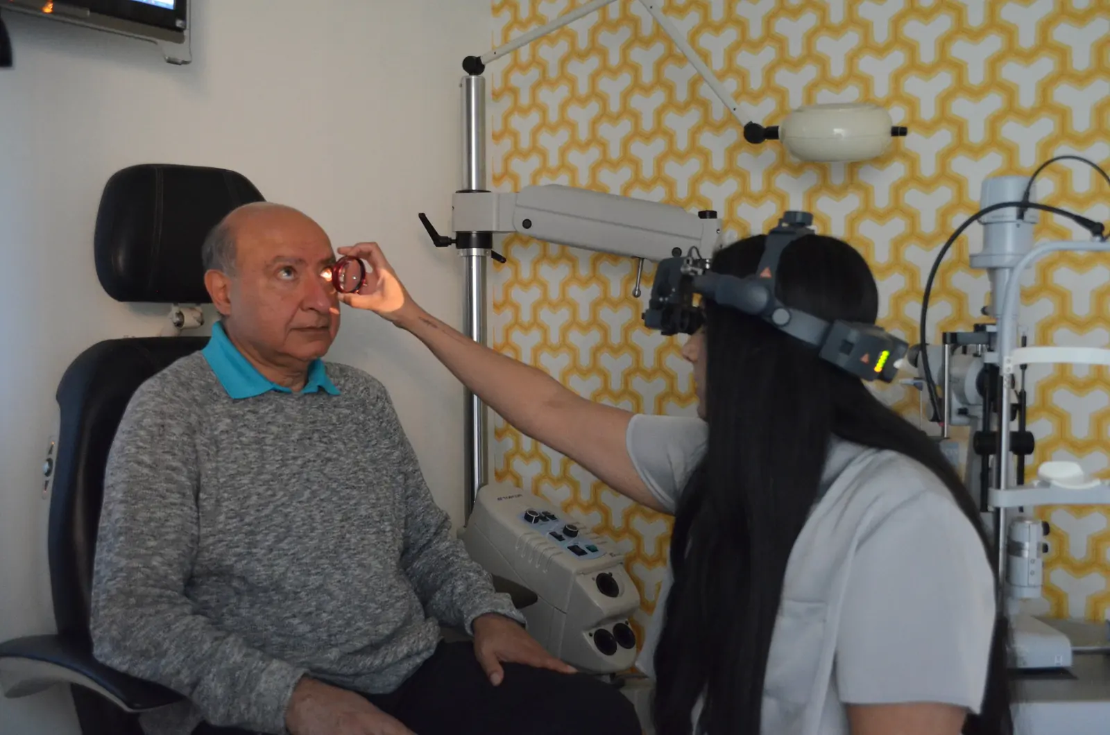 An optometrist uses a headset ophthalmoscope and a hand-held lens to examine a patient’s eye at The EyeSite