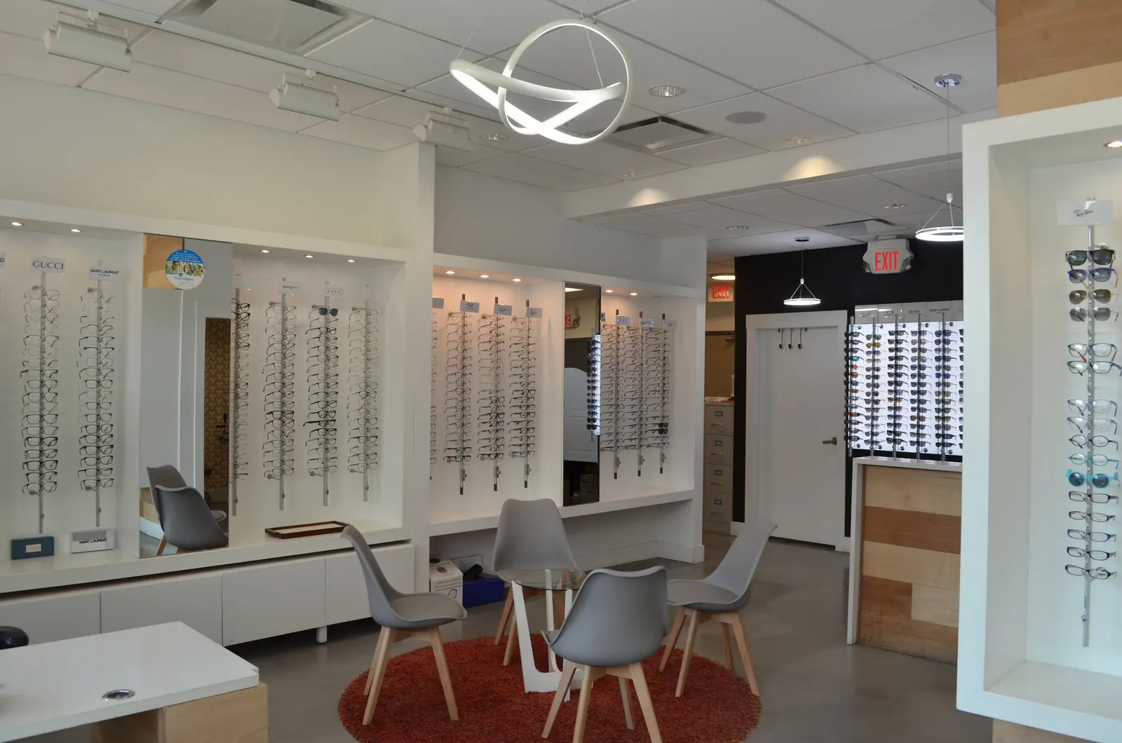 The optical at The EyeSite: lit frame displays along white walls, a ring pendant light and grey chairs on a round rug